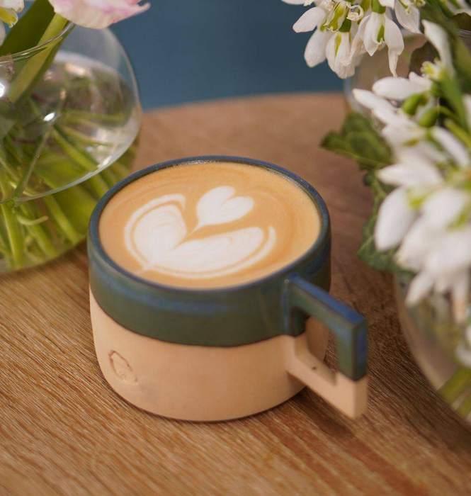 Cană de cafea cu latte art, printre flori albe